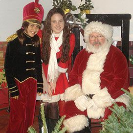 santa seated with helper in drummer outfit and one in a fur-trimmed red mini dress