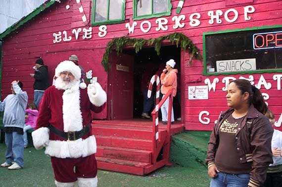 santa standing in front of  the elves workshop, a red building with green trim